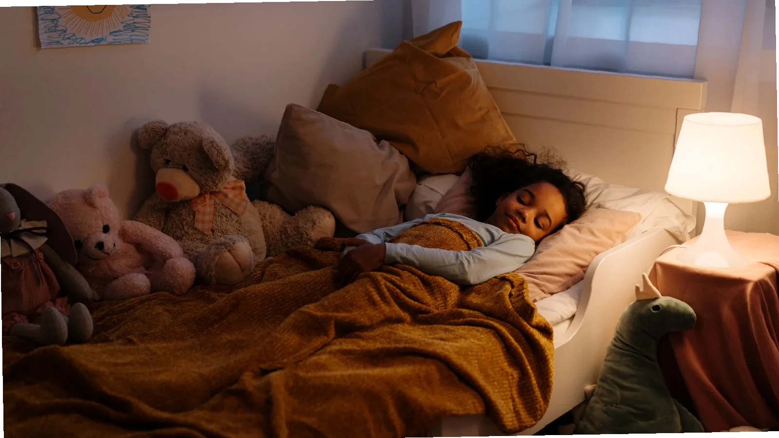 Tired parent adjusting a toddler bedtime blanket setup in a dimly lit bedroom