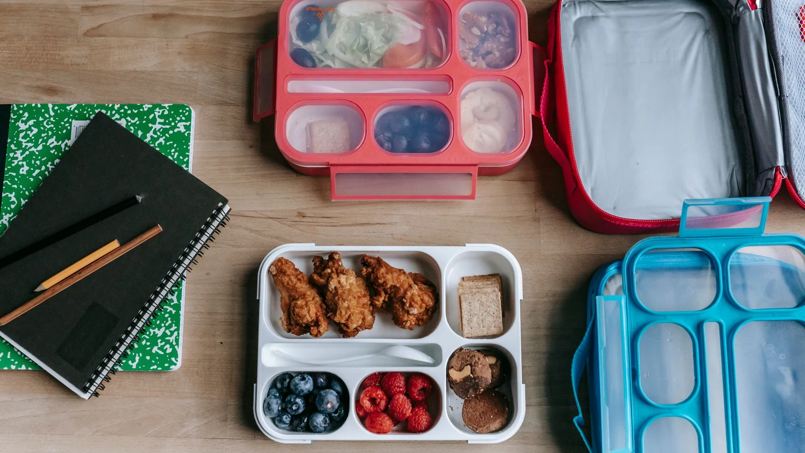 Packed school lunch containers on a table beside notebooks