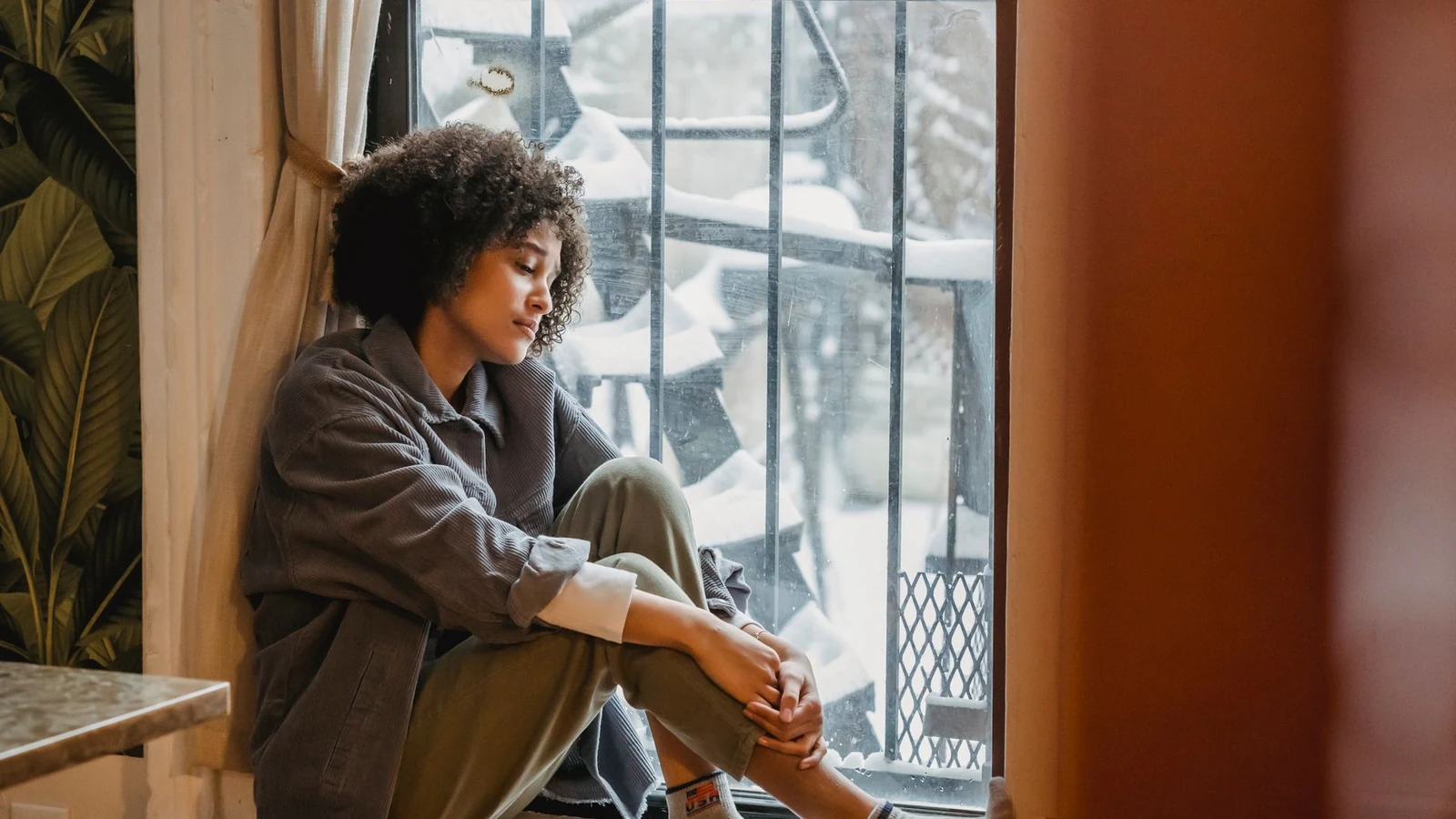 A woman sitting on a windowsill in low seasonal light, worn out