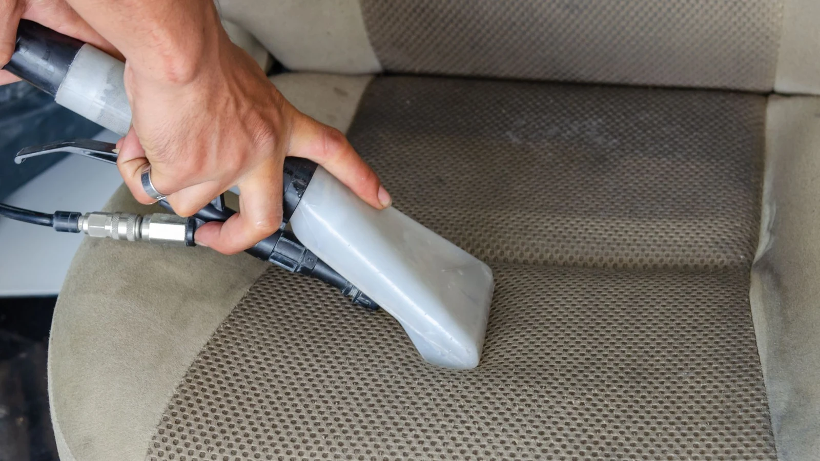 A hand pressing a handheld upholstery extraction tool into a stained car seat cushion, mid-clean
