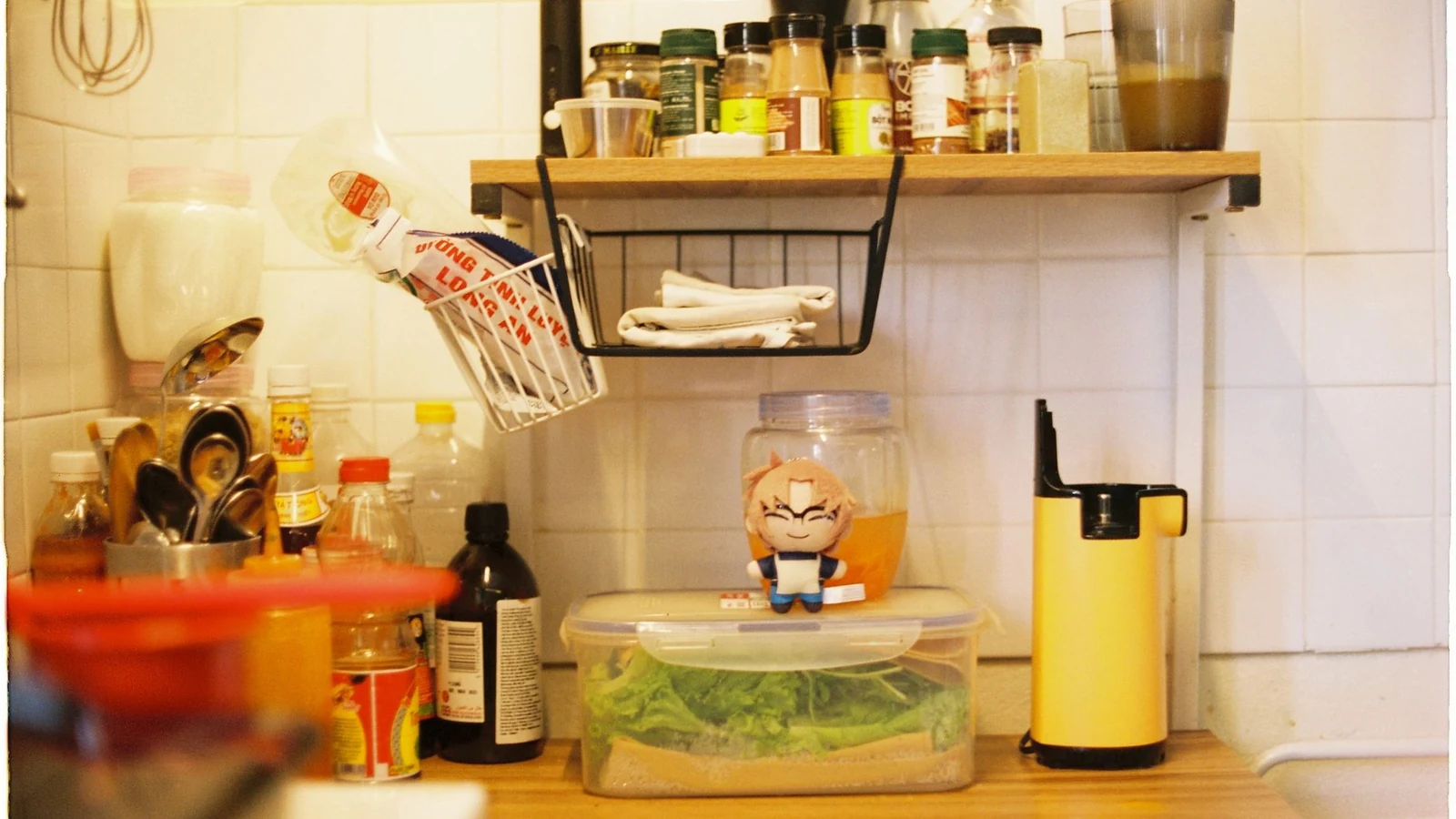 A small kitchen counter crowded with jars, utensils and a shelf above