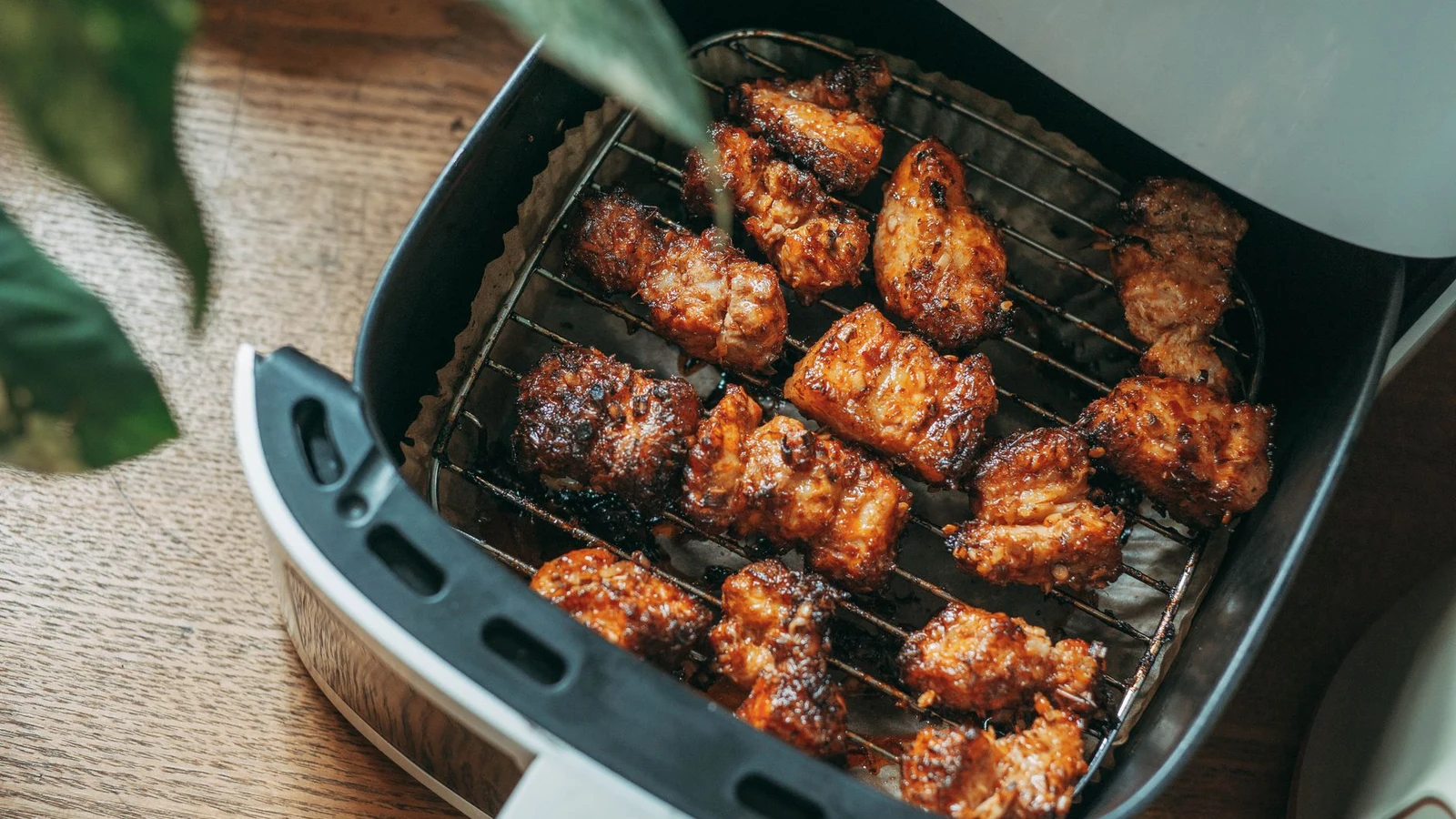 Crisped chicken pieces cooking on the rack of an electric air fryer basket in a home kitchen