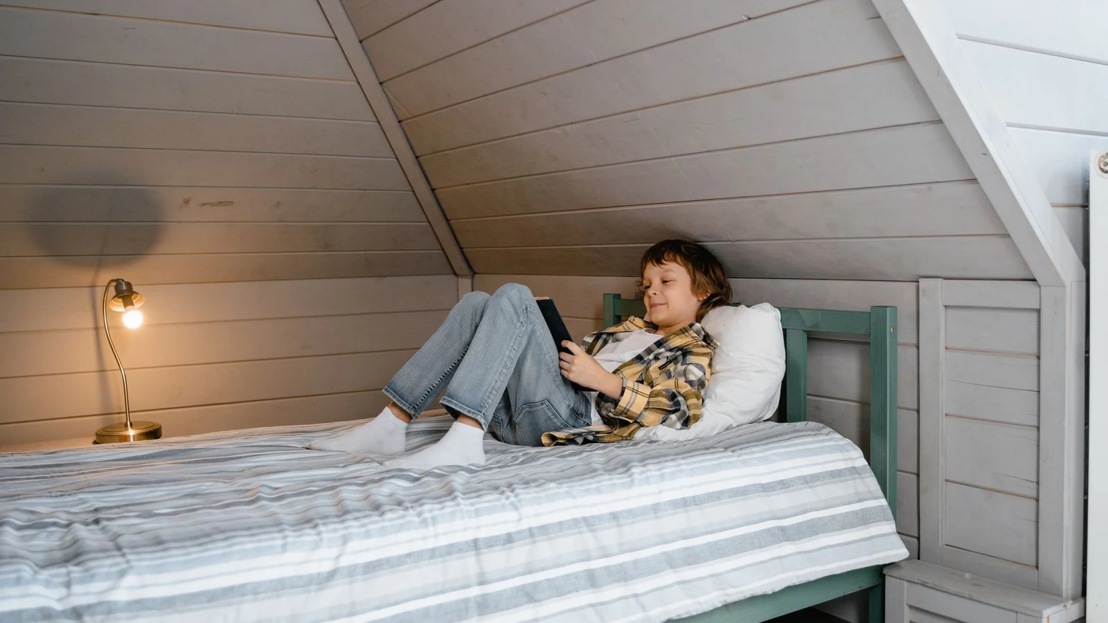 A child lying awake on a bed with daylight still at the window