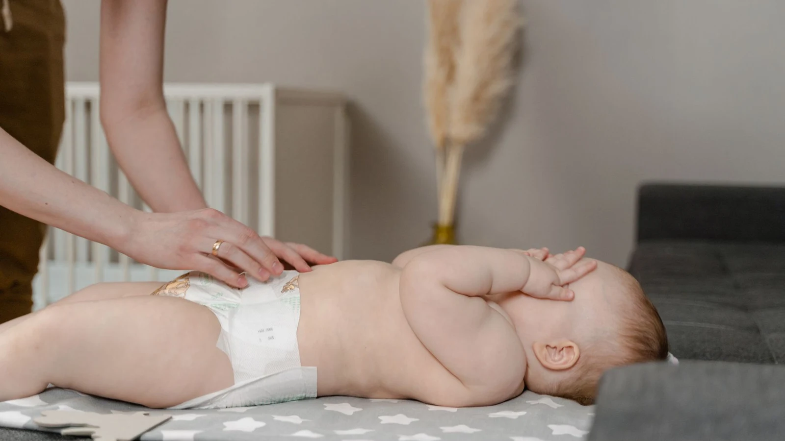 Newborn baby boy on a changing pad during a diaper change, with a washcloth and petroleum jelly staged nearby