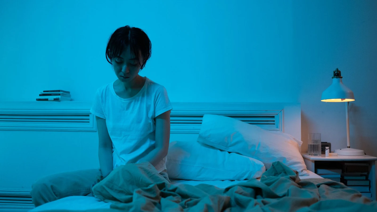 One parent sitting alone in a lamplit kitchen after the children are in bed, with the day's dishes still out