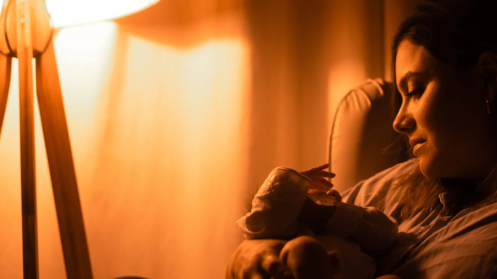 Mother cradling her baby close in a dim, lamp-lit room during a calm bedtime wind-down